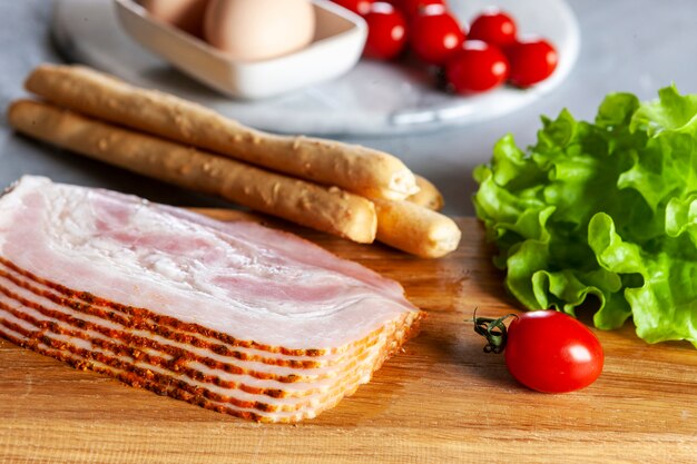 Traditioneel pancetta-spek geserveerd met gepekelde olijven, tomaten, groene sla, eieren en grissinibrood, ingrediënten voor het ontbijt