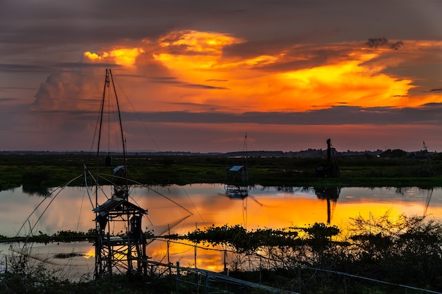 Traditioneel visgereedschap of bamboe visval op zonsonderganglicht, landschapssilhouet.