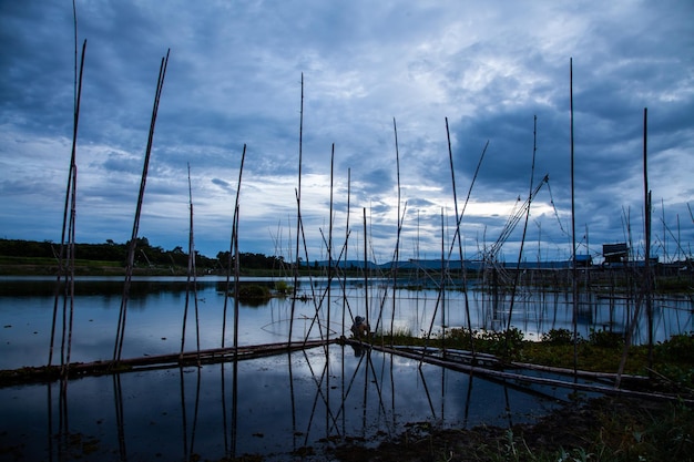 Traditioneel visserijhulpmiddel of bamboevissenval op het silhouet van het zonsonderganglichtlandschap