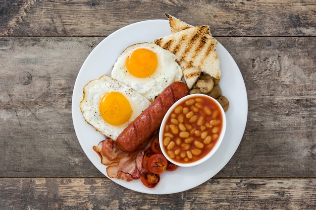 Traditioneel volledig Engels ontbijt met gebakken eieren, worstjes, bonen, champignons, gegrilde tomaten en spek op houten oppervlak