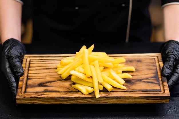 Traditionele Amerikaanse fastfoodrestaurantsnacks. Bijgesneden schot van chef-kok met portie frietjes op een houten bord.