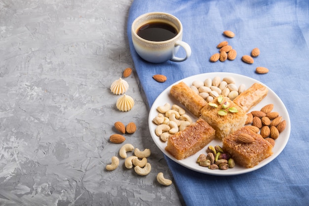 Traditionele arabische snoepjes (basbus, kunafa, baklava), een kopje koffie en noten op een grijze betonnen oppervlakte zijaanzicht, kopie ruimte.