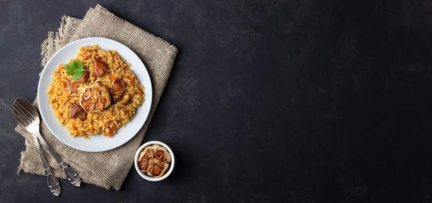 Foto traditionele aziatische schotel - pilaf van rijst, groenten en vlees in een bord op zwarte achtergrond. bovenaanzicht. lang formaat.