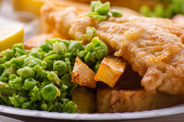 Foto traditionele britse streetfood fish and chips met papperige erwten op papieren bord