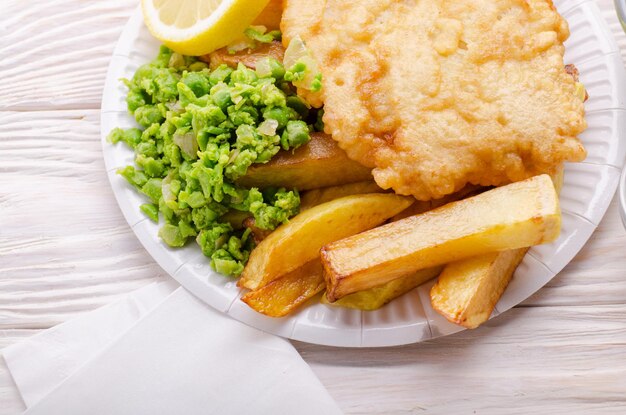 Traditionele Britse streetfood fish and chips met papperige erwten op papieren bord