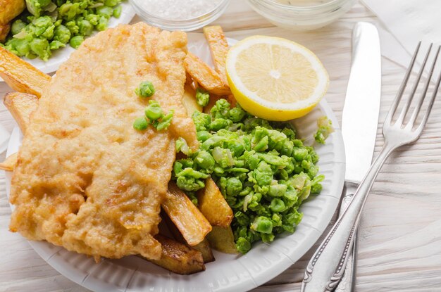 Traditionele Britse streetfood fish and chips met tartaarsaus en papperige erwten op papieren bord