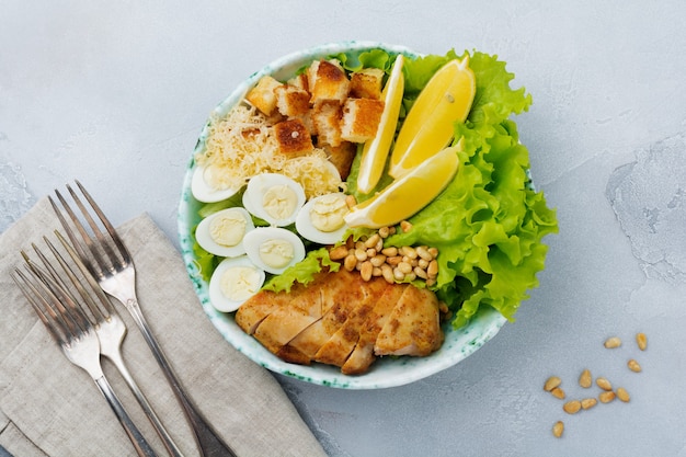 Traditionele Caesarsalade met kwarteleitjes en pijnboompitten in een lichte ceramische kom op een grijze steen of concrete achtergrond.