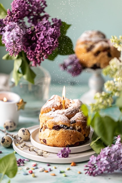 Traditionele cupcake pasen cake kraffin met rozijnen en poedersuiker op tafel. pasen taarten, kaarsen en een boeket van lila bloemen.