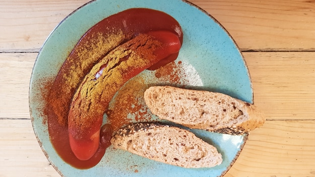 Foto traditionele duitse curryworst in een bord op een houten tafel in een café met brood. uitzicht van boven. specialiteiten van duitsland en berlijn. worst in pittige tomaten-rode currysaus.