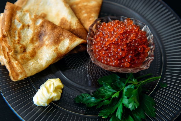 Traditionele dunne Russische pannenkoeken met rode kaviaar, boter en groenten