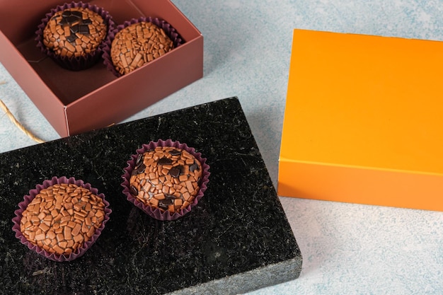 Traditionele en bittere brigadeiros op een zwarte marmeren steen naast een oranje doos