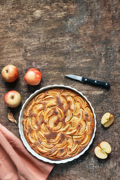 Traditionele franse zelfgemaakte appeltaart in een witte keramische bakvorm op houten achtergrond bovenaanzicht