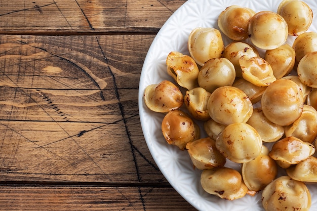 Traditionele gebakken pelmeni, ravioli, dumplings gevuld met vlees op plaat, Russische keuken. Houten rustieke tafel, kopie ruimte.