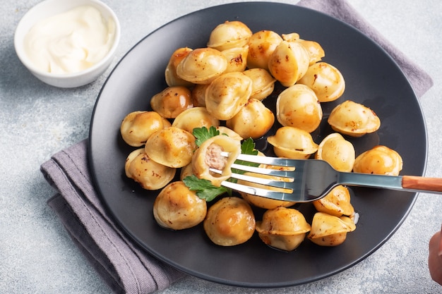 Traditionele gebakken pelmeni, ravioli, dumplings gevuld met vlees op zwarte plaat, Russische keuken. Grijze betonnen tafel, kopie ruimte.