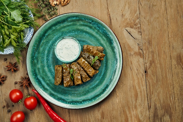 Traditionele Georgische dolma - rijst met gehakt in druivenbladeren op een blauw bord met yoghurt saus. Houten oppervlak. Bovenaanzicht. Sarma