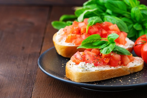 Traditionele geroosterde italiaanse tomatenbruschetta met kruiden en basilicum op donkere houten plank