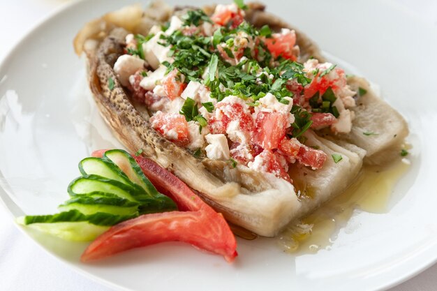 Foto traditionele griekse gebakken aubergines gevuld met gemengde feta zoete peper en groenten bedekt met olijfolie geserveerd op een wit bord in een restaurant