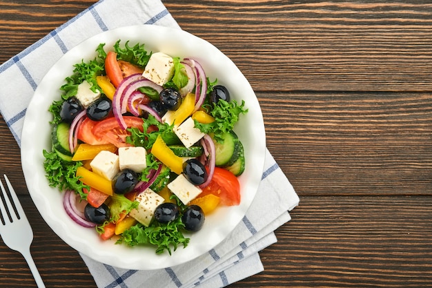 Traditionele Griekse salade van verse komkommer, tomaat, paprika, sla, rode ui, fetakaas en olijven met olijfolie op wit bord. Gezonde voeding, bovenaanzicht.