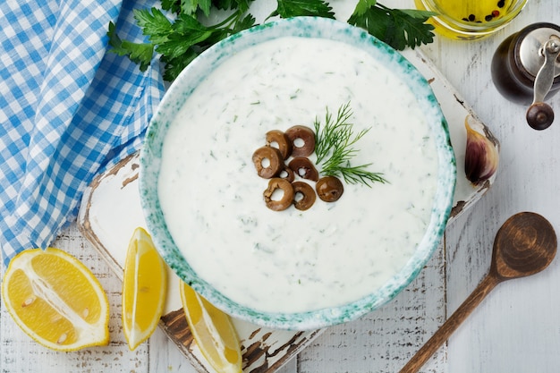 Traditionele Griekse saus Tzatziki. Yoghurt, komkommer, dille, knoflook en zoute olie in een keramische kom op een licht houten oppervlak