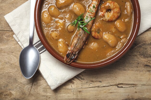 Traditionele huisgemaakte witte bonenstoofpot met garnalen. typisch spaans eten. op houten tafel