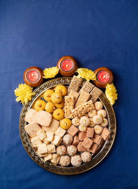 Traditionele Indiase zoetigheden op blauwe achtergrond met kaarsen en bloemen plat gelegd