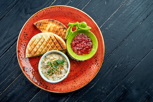 Traditionele Israëlische of oosterse Baba ghanoush met groentesalsa en pitabroodje, geserveerd in een rood bord op houten tafel
