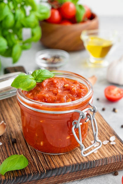 Traditionele Italiaanse Marinara-saus in een pot op een betonnen ondergrond met kruiden en ingrediënten