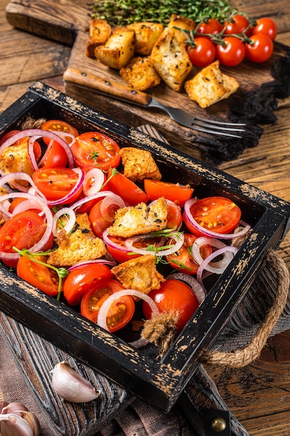 Foto traditionele italiaanse panzanella-salade met tomaten, ui en broodcroutons in houten dienblad. houten achtergrond. bovenaanzicht.