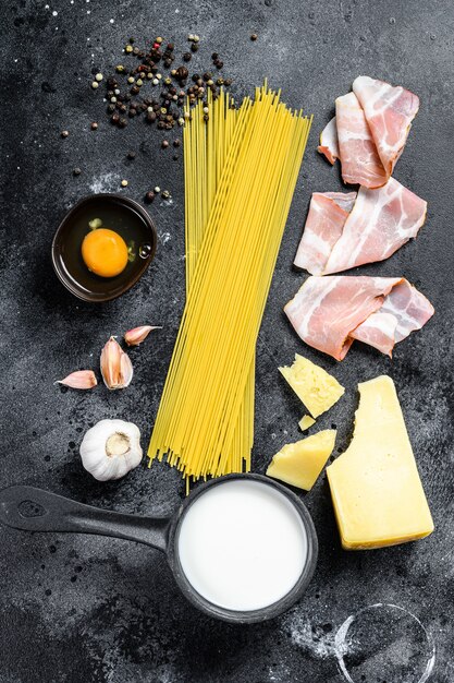 Traditionele Italiaanse Pasta Carbonara-ingrediënten. Spek, Spaghetti, Parmezaanse kaas en pecorino kaas, ei, knoflook. Zwarte achtergrond.