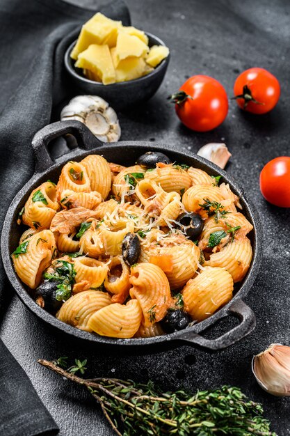 Traditionele Italiaanse pasta met tomaat, olijven, kappertjes, ansjovis. Conchiglie rigate, puttanesca op zwart. Bovenaanzicht