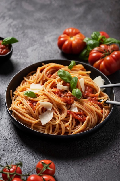 Traditionele Italiaanse pasta met tomatensaus, basilicum en kaas op de zwarte achtergrond, bovenaanzicht met kopie ruimte