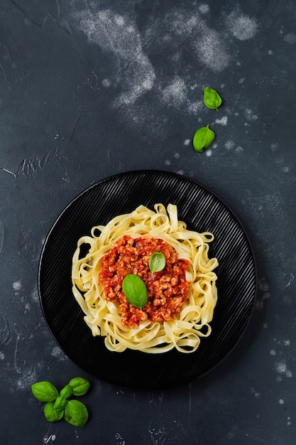 Traditionele Italiaanse schotel fettuccine pasta met bolognese saus, basilicum en Parmezaanse kaas in zwarte plaat op donkere houten oppervlak. Bovenaanzicht