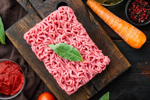 Traditionele Italiaanse tomatensaus bolognese met ingrediënten gehakt vlees tomaat en kruiden op houten snijplank op oude donkere houten tafel achtergrond bovenaanzicht plat lag