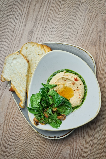 Traditionele kikkererwten hummus in kom met salade, brood, aubergine en champignons. Israëlische keuken. Snack. Houten achtergrond