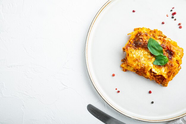 Traditionele lasagne gemaakt met rundergehakt bolognese saus gegarneerd met basilicumbladeren op plaat op witte stenen tafelblad weergave plat leggen