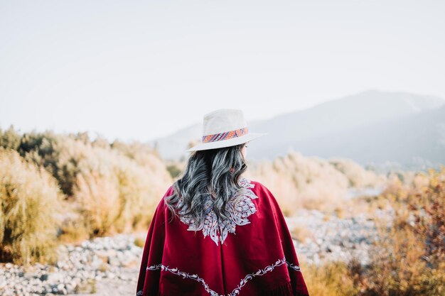 Traditionele Latijns-Amerikaanse vrouw met een rode poncho en een hoed van achteren gezien in een natuurlijke ruimte