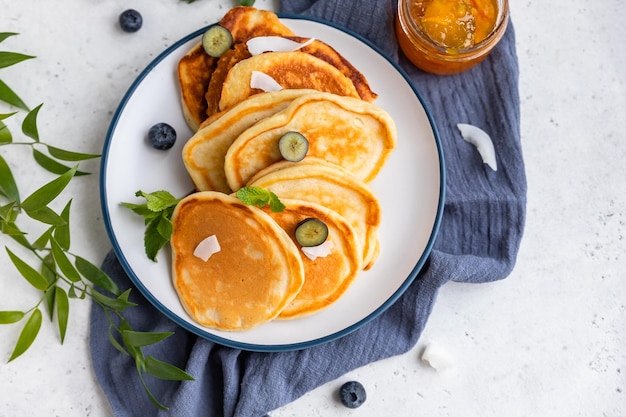 Traditionele luchtige pannenkoeken met sinaasappeljam, bosbessen, kokoschips en munt voor een gezond ontbijt