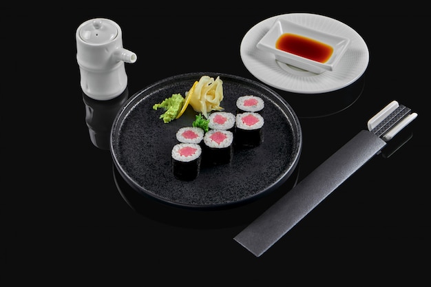 Traditionele maki sushi rolt met tonijn op een zwarte plaat in samenstelling met sojasaus en eetstokjes op een zwarte ondergrond. Japans eten. Foto voor het menu