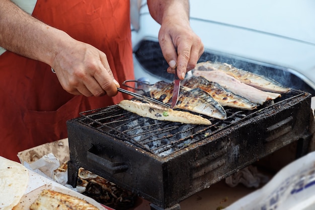 Traditionele mediterrane keuken. De mens roostert witte vissenbalyk bij straatmarkt, handenclose-up. Hij draait vis en pelt de schaal af. Lokaal straatvoedsel in Turkije.