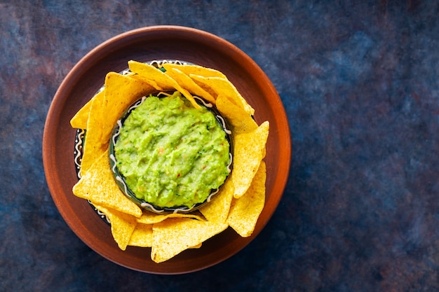 Traditionele Mexicaanse sausguacamole met tortillachips in kleikom. Kom guacamole met nachos chips op een donkere achtergrond. Ruimte kopiëren. Bovenaanzicht