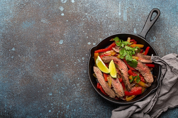 Traditionele Mexicaanse schotel Beef fajitas met paprika in zwarte gietijzeren pan op rustieke stenen achtergrond van bovenaf met ruimte voor tekst, Amerikaans Mexicaans eten