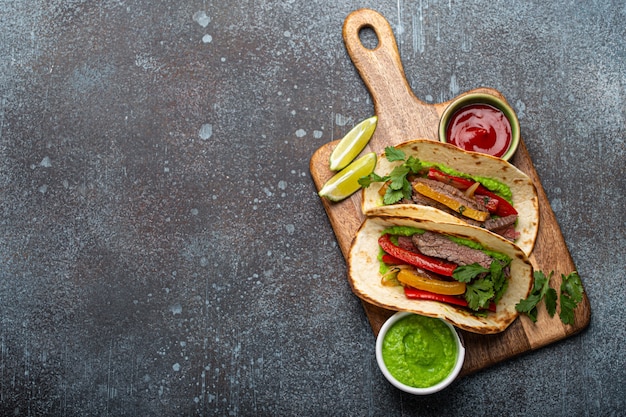 Traditionele Mexicaanse schotel Beef fajitas taco's geserveerd op houten snijplank met tomatensalsa en guacamole op rustieke stenen achtergrond van bovenaf met ruimte voor tekst, Amerikaans Mexicaans eten