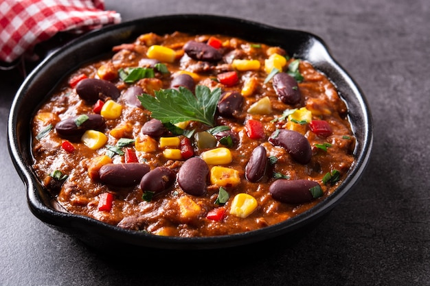 Traditionele Mexicaanse tex mex chili con carne in ijzeren pan op zwarte stenen achtergrond