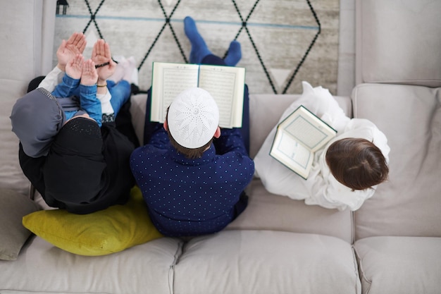 Traditionele moslimfamilieouders met kinderen die de Koran lezen en samen op de bank bidden voor het iftar-diner tijdens een ramadanfeest thuis bovenaanzicht