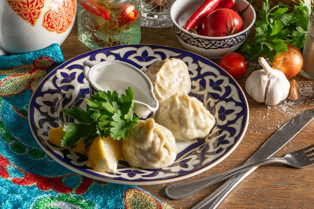 Traditionele oezbeekse handgemaakte manti gestoomd met lamsgehakt en uienvulling met een oosterse saus gemaakt van zure room, zout, peper en knoflook op een bord met een traditioneel oezbeeks patroon