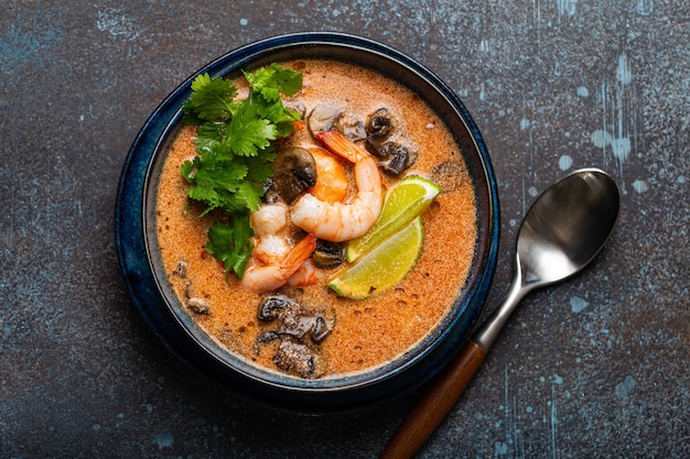 Traditionele pittige Thaise soep Tom Yum met garnalen en zeevruchten in keramische kom op blauwe steen rustieke achtergrond van bovenaf, klassiek gerecht uit de keuken van Thailand