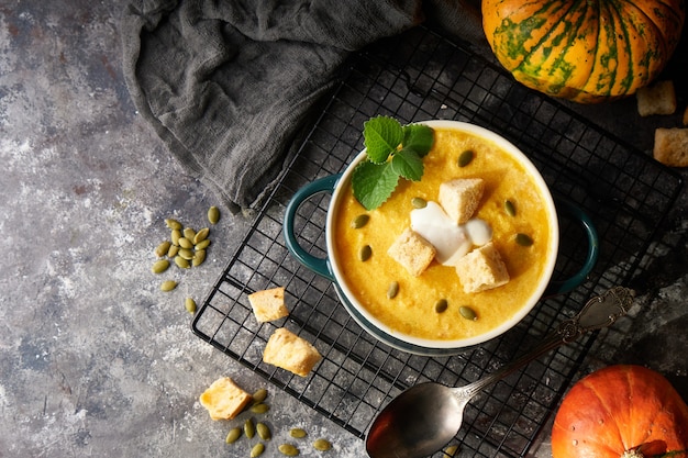 Traditionele pompoensoep puree met crackers, room en zaden in een kom, op een donkere achtergrond Kopieer de ruimte