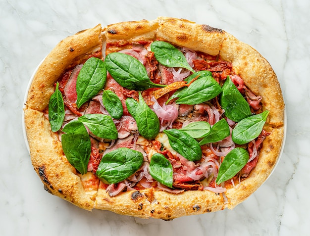 Traditionele Romeinse pizza met rosbief, zongedroogde tomaten, ingelegde ui en spinazie