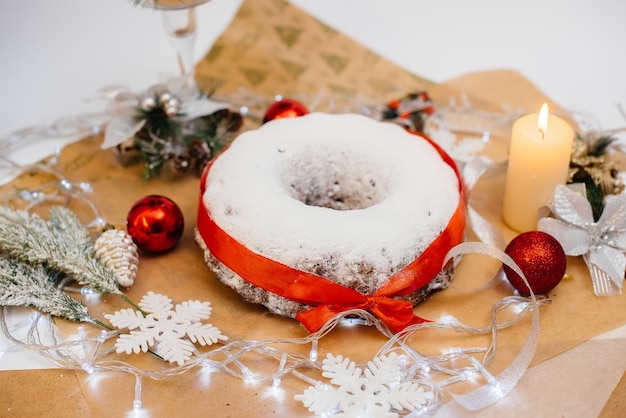 Traditionele ronde kerststol gemaakt van gedroogde vruchten en noten bestrooid met poedersuiker op de achtergrond van een kerstdecor met kaarsen. Traditionele kerst cupcake.