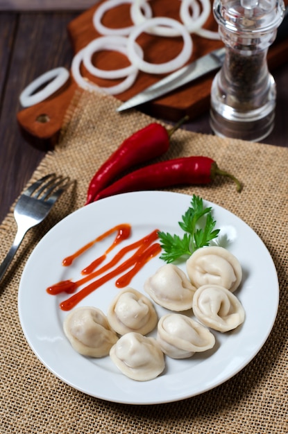 Traditionele Russische dumplings, ravioli, bollen op een witte plaat met rode saus en peterselie.